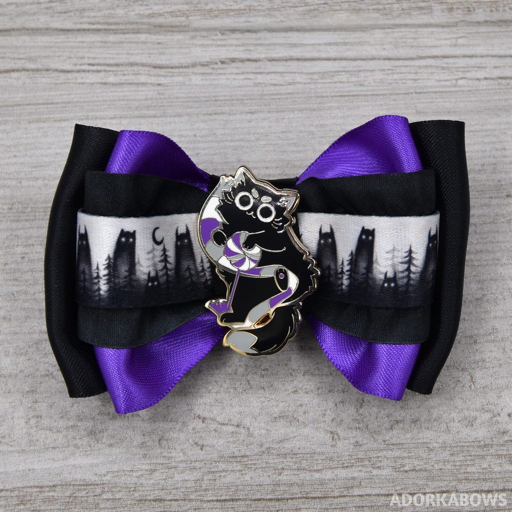 a cat themed hair bow in Asexual pride colors which includes a black cat pin at the center holding a scarf of white, gray and purple.
