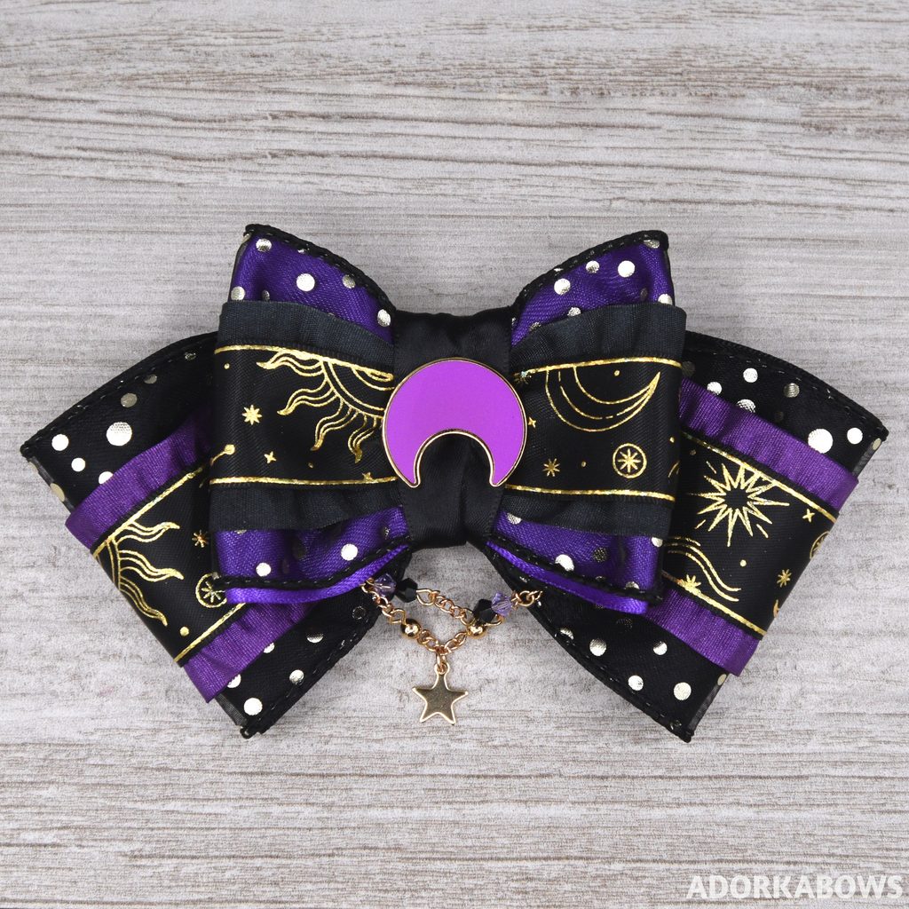 A purple and black hair bow with gold start motif ribbon, ruffles, a center pin of an upsidedown purple crescent moon and some dangling chains with matching gems and a star. Pin by me.